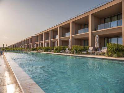 Moderner Hotelkomplex mit langem Pool und Balkonen bei Sonnenuntergang.
