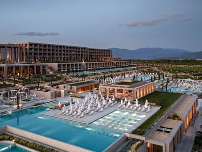 Moderner Hotelkomplex mit beleuchteten Pools und Liegestühlen bei Dämmerung.