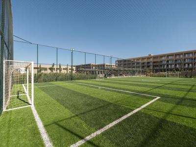Ein Fußballfeld mit grünem Kunstrasen neben einem Hotelgebäude unter klarem Himmel.