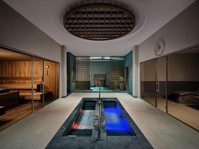 Moderner Wellnessbereich mit Sauna und zwei beleuchteten Wasserbecken im Innenbereich.