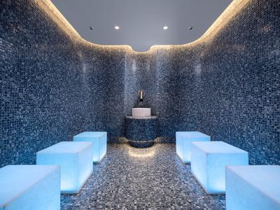 Moderner Spa-Raum mit blauen beleuchteten Sitzwürfeln und dunklen Mosaikwänden.