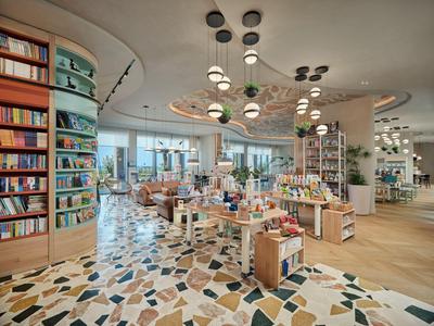 Heller Hotel-Laden mit Büchern, Souvenirs und modernen Lampen auf buntem Boden.