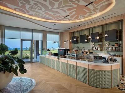 Modernes Café mit großer Theke, Pflanzen und Blick auf das Meer durch Panoramafenster.