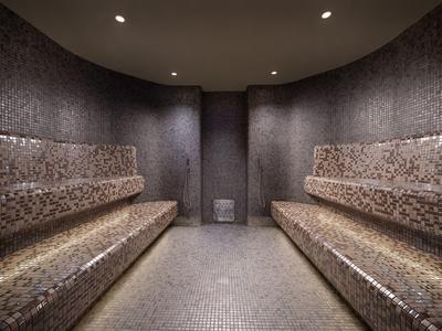 Sauna mit zwei Reihen von Mosaikfliesenbänken an den Wänden und gedämpftem Licht.