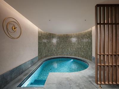Moderner Hotelpool mit blauem Wasser, Mosaikfliesen und dekorativer Holzabtrennung.