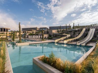 Moderner Hotelpool mit Wasserrutschen und Liegestühlen unter blauem Himmel.
