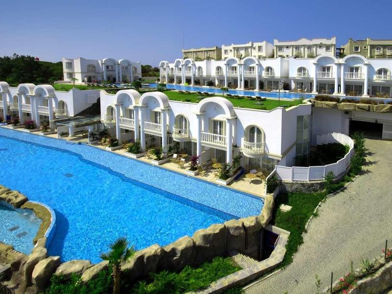 Großes Hotel mit weißem Gebäude, blauem Pool und grüner Landschaft unter klarem Himmel.