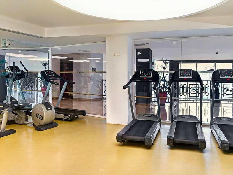 Moderner Fitnessraum mit Laufbändern, Fahrrädern und großen Fenstern bei Tageslicht.