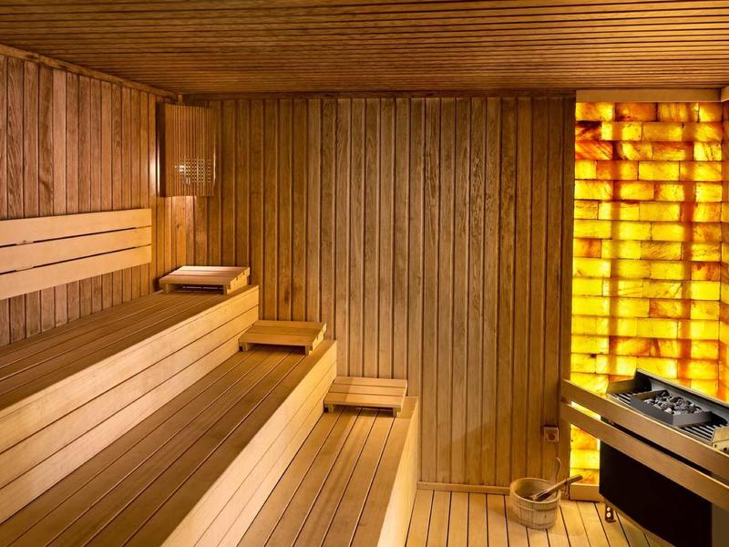 Innenraum einer Holzsauna mit mehrstufigen Bänken und beleuchteten salzsteinverkleideten Wänden.