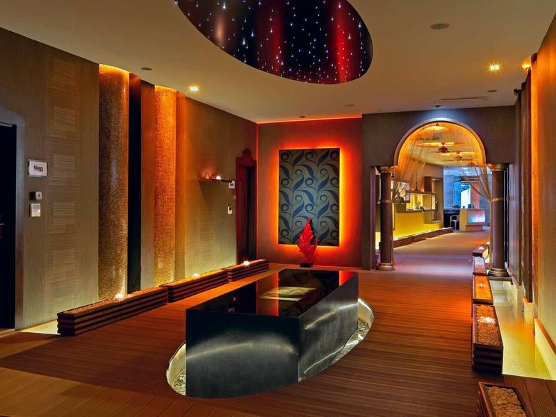 Luxuriöser Hotelflur mit warmem Licht, weichem Teppich und moderner Sitzgruppe unter beleuchtetem Deckenfenster.