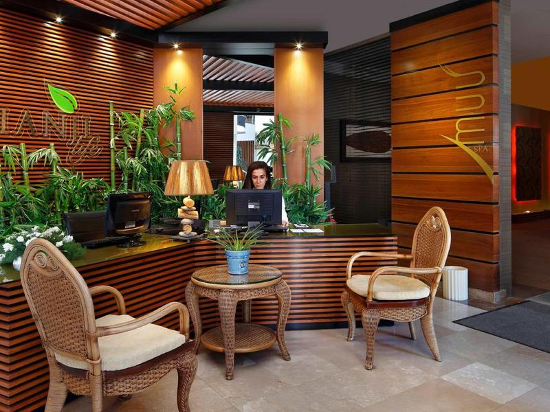 Moderne Hotelrezeption mit Holzmöbeln, Pflanzen, zwei Sesseln und einem runden Tisch in warmem Licht.