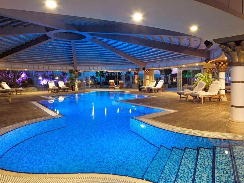 Großer, beleuchteter Pool mit geschwungener Form, umgeben von weißen Säulen und gemütlichen Sitzbereichen.