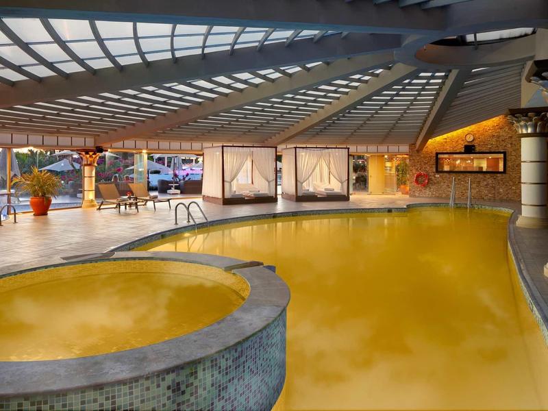 Innenbad mit gelbem Wasser, Whirlpool, großen Fenstern und Segelboot-Bildern an der Wand.