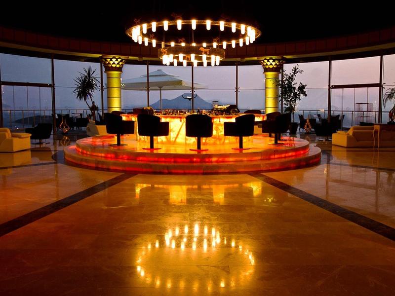 Runde Bühne mit schwarzen Stühlen, goldgelber Beleuchtung und großen Fenstern im Hintergrund.