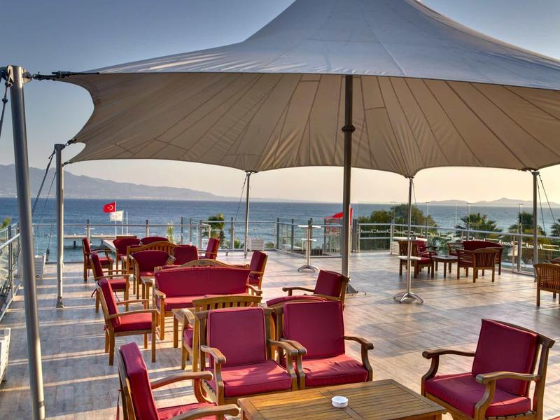 Rooftop terrace with red seating and a large sunshade overlooking the sea at sunset.
