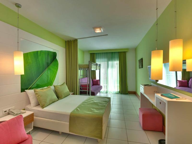 Modern hotel room with green color scheme, large bed, and desk with lamps.