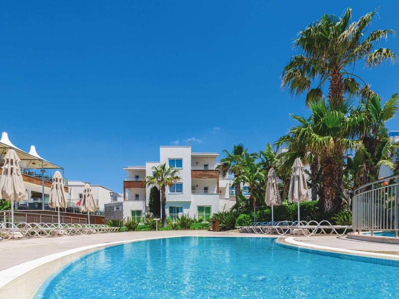 Round hotel pool with sun loungers and palm trees under clear blue sky