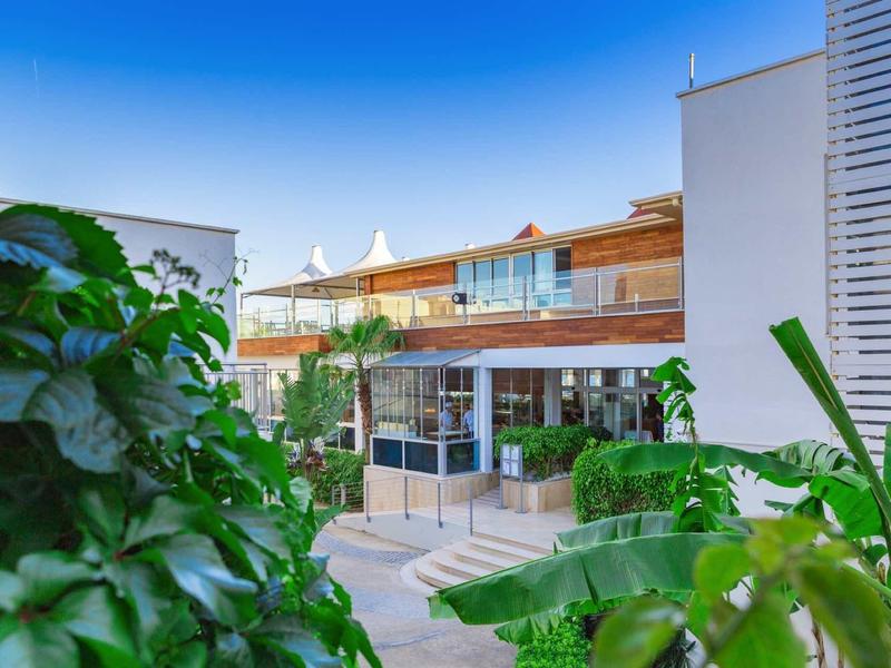 Modern hotel complex with terraces and abundant greenery under clear sky.