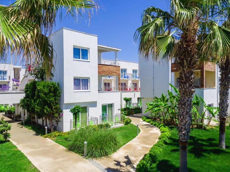 Modern holiday apartment with palm trees and well-kept garden under blue sky.