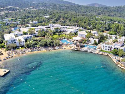 View of a coastal hotel with pools and beaches by forested hills.