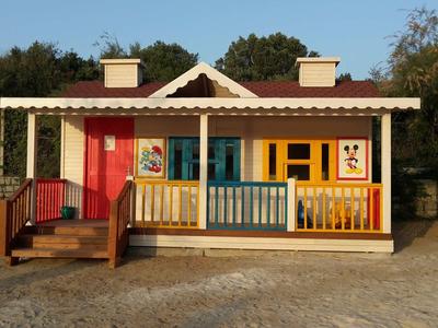 Small colorful vacation house with porch and three vibrant doors in a sunny setting.