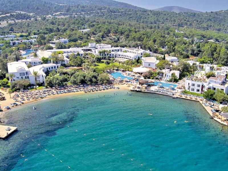 View of a coastal hotel with pools and beaches by forested hills.