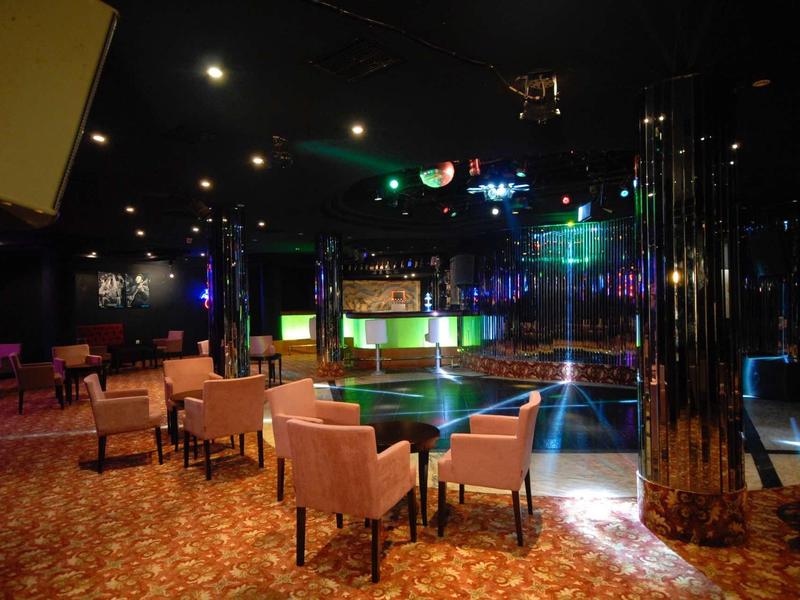 Empty dance floor with round tables and padded chairs in a club with colorful lighting.