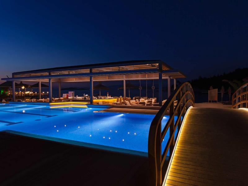 Illuminated hotel pool at night with seating area and clear night sky.
