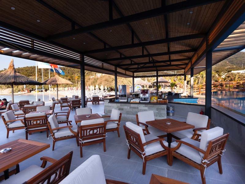 Open seating area with wooden furniture and sun umbrellas by the sea at sunset.