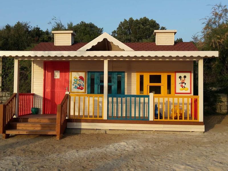 Small colorful vacation house with porch and three vibrant doors in a sunny setting.