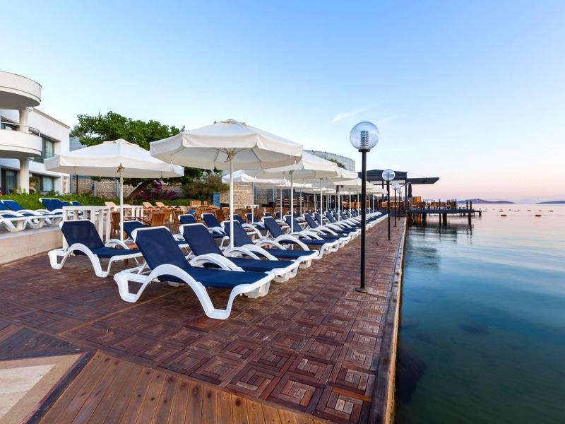 Empty lounge chairs and umbrellas on a wooden pier by the calm sea.