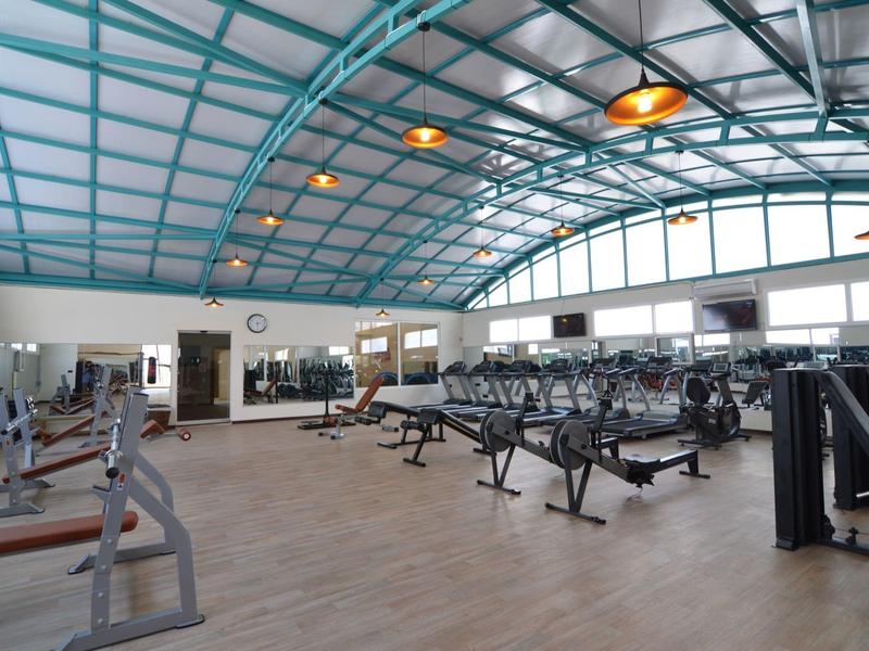 Großer, heller Fitnessraum mit blauer Decke, vielen Geräten und Holzboden.