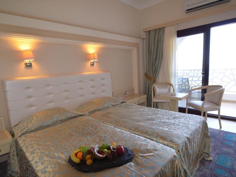 Ein helles Doppelzimmer mit zwei Einzelbetten, weißem Kopfteil, Tisch und Balkon mit Geländer.