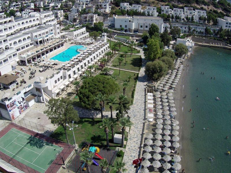 Strandresort mit Pool, Tennisplatz, Sonnenschirmen am Sandstrand und blauem Meer.