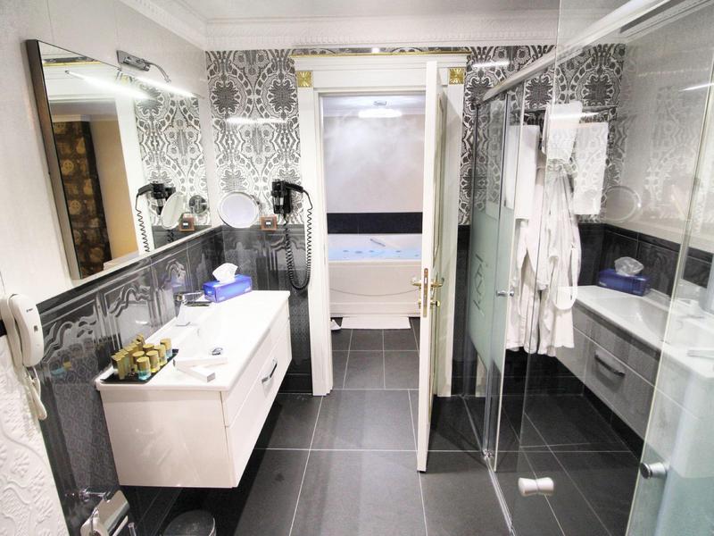 Modernes, weiß-graues Badezimmer mit Dusche, Waschbecken, großem Spiegel und Badewanne im Hintergrund.