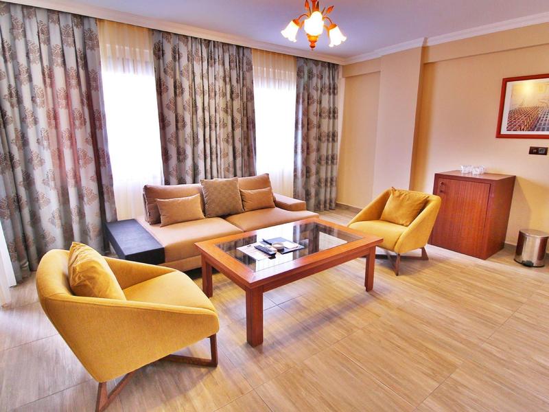 Wohnzimmer mit gelben Sesseln, braunem Sofa, Holztisch und Vorhängen in Beige- und Brauntönen.