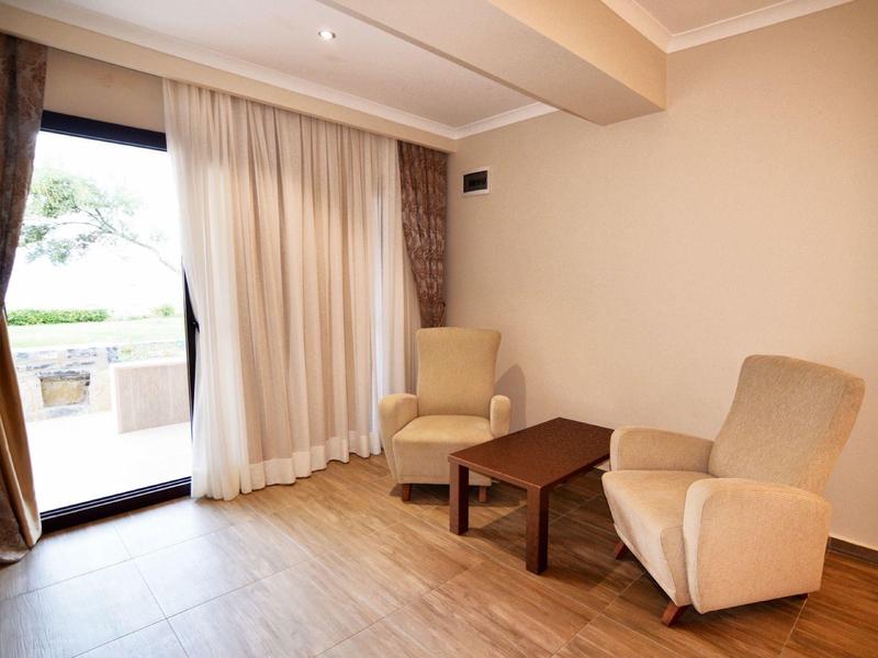 Gemütliches Zimmer mit zwei beigen Sesseln, Holztisch und großem Fenster mit Vorhängen.