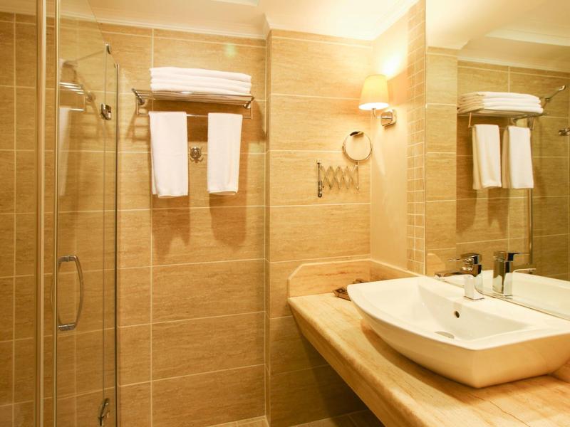 Helles Badezimmer mit Glas-Dusche, Handtüchern, großem Spiegel und weißem Waschbecken auf Holzplatte.