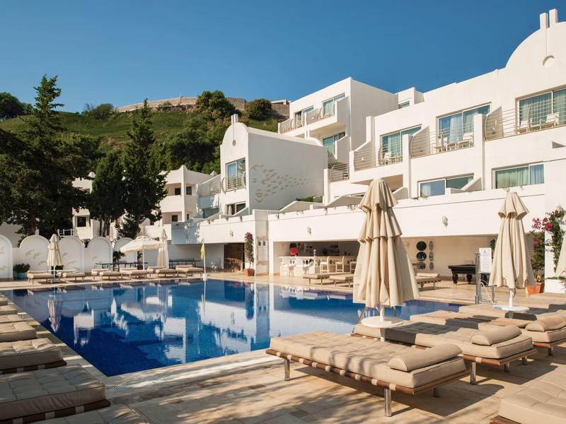 Piscina moderna de hotel con tumbonas y sombrillas en un entorno soleado.