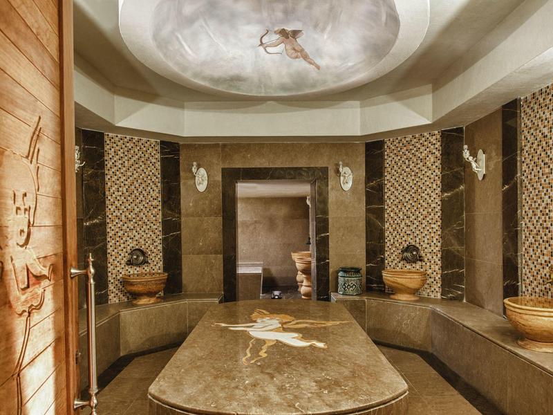 Sala de bienestar elegante con banco de mármol y decoración artística en el techo en tonos cálidos.