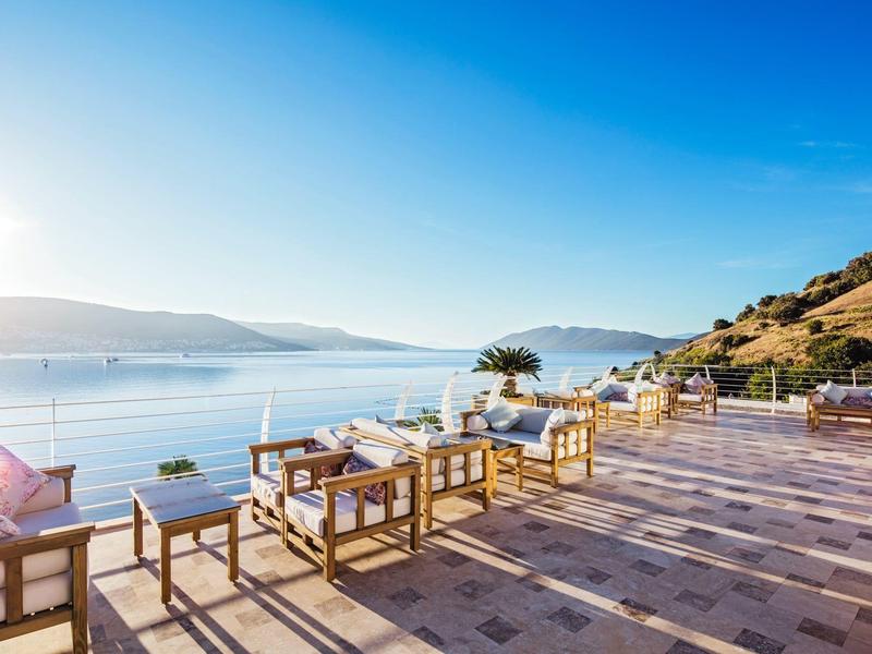 Gran terraza con sillas y mesas con vistas al mar y colinas bajo un cielo despejado.