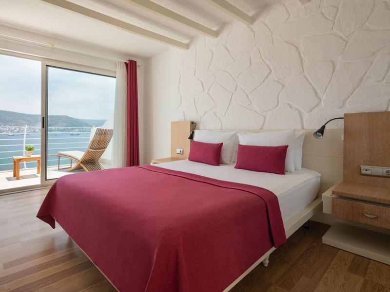 Dormitorio con cama doble, ropa de cama roja y balcón con vistas al mar.