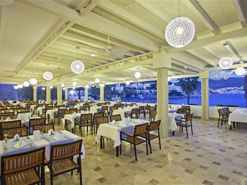 Restaurante abierto y elegante junto al agua con manteles blancos y sillas de madera al atardecer.