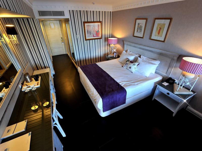 Elegancki pokój hotelowy z podwójnym łóżkiem, fioletowymi lampami i ciemnym biurkiem.