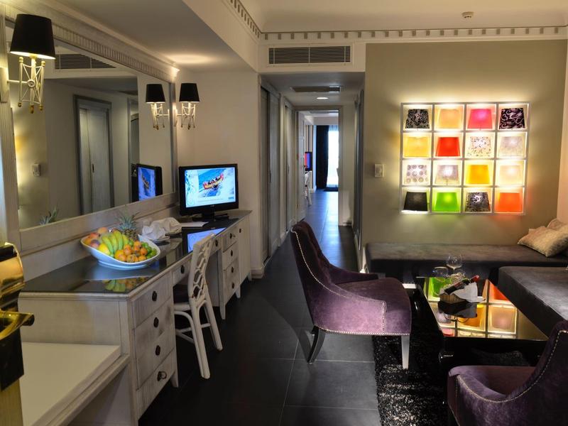 Elegancki salon z fioletowymi sofami, telewizorem, lustrem i kolorowymi kwadratami na ścianie.