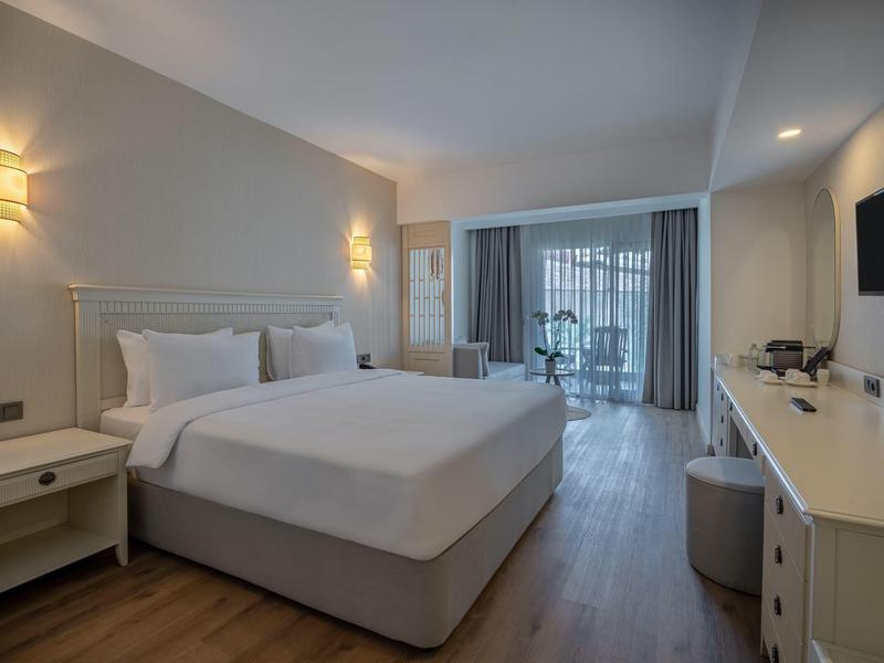 Nowoczesny pokój hotelowy z dużym łóżkiem, biurkiem, telewizorem i przeszklonym balkonem.