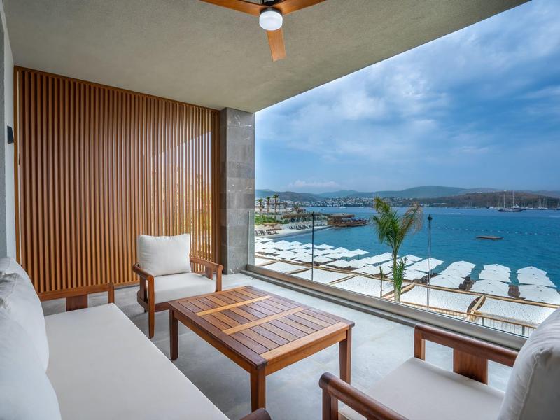 Taras pokoju hotelowego z widokiem na morze, drewniane meble i białe poduszki.