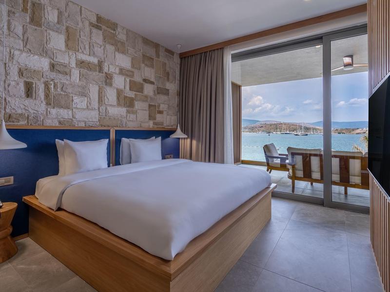 Nowoczesny pokój hotelowy z podwójnym łóżkiem, kamienną ścianą, balkonem z widokiem na morze.