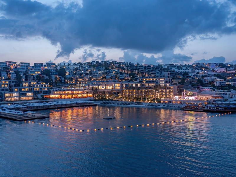 Nocny widok na oświetlone miasto nadbrzeżne z portem i budynkami nad wodą.