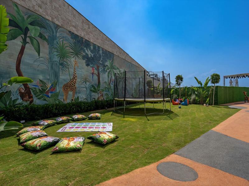 Zewnętrzny plac zabaw z poduszkami, trampoliną i trawnikiem pod niebieskim niebem.